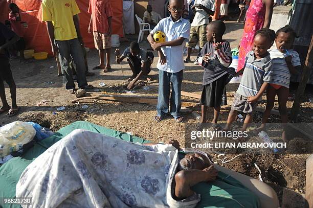 Children look at a Haitian elderly sick man laying on his mattres while his relatives fix their tent on February 16, 2010 at a camp in Port-au-Prince...