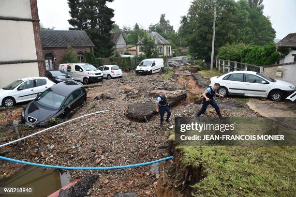 French gendarmes walk on a road destroyed by floodwaters on June 6, 2018 in the French northwestern city of Breteuil, after the Iton river burst its...