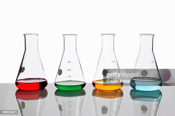 four beakers holding different colored fluids - bouteille d'erlenmeyer photos et images de collection