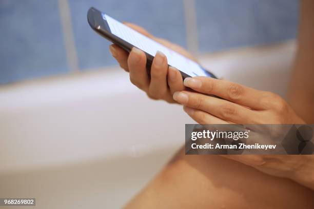 woman taking a bath and using smartphone - arman zhenikeyev stock-fotos und bilder