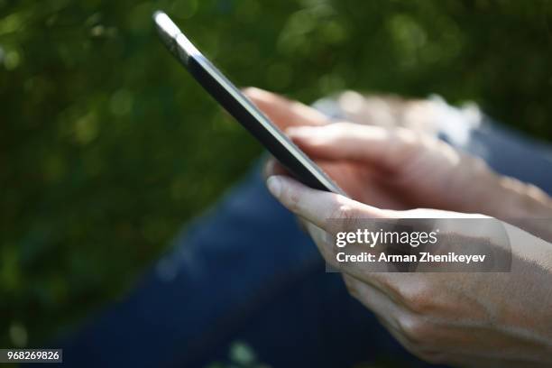 woman with tablet computer sitting outdoors - arman zhenikeyev photos et images de collection