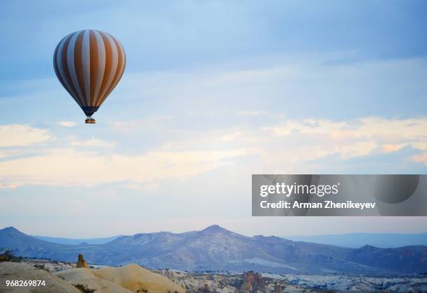 hot air balloon flying over the rocky land. cappadocia, turkey - arman zhenikeyev stock-fotos und bilder