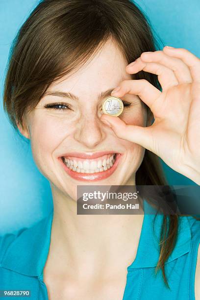 young woman holding up euro coin over eye, smiling - one euro coin stock pictures, royalty-free photos & images