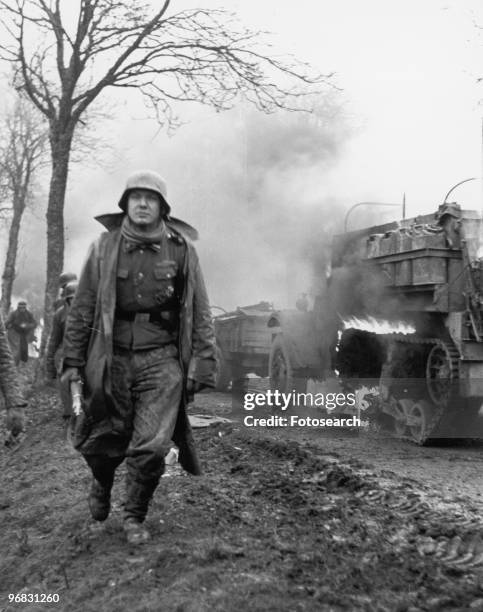 Photograph of a German Soldier passing a Blazing American Half-Track on the Second Day of the German Ardennes Offensive, December 17th, 1944.