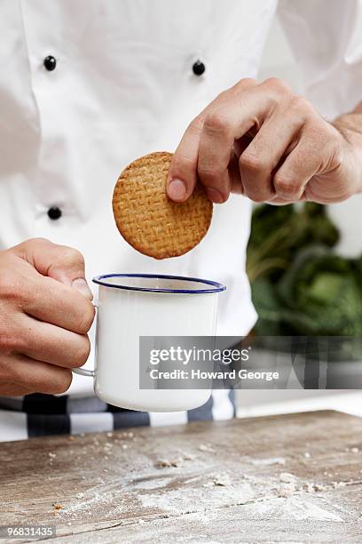 chef dunking biscuit into mug of tea - man hand holding cookie photos et images de collection