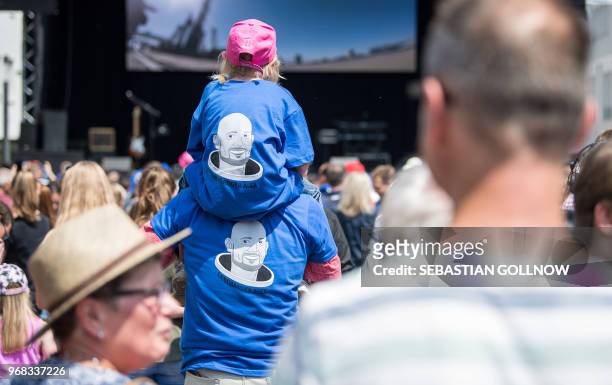 Man carrying a child on his shoulders, both wearing shirts with the portrait of German astronaut Alexander Gerst, watch the start of a Soyuz...