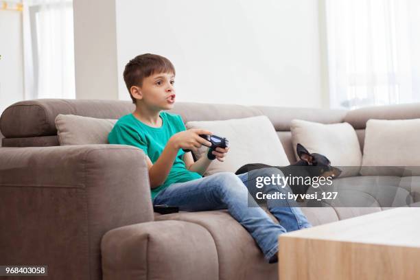 boy, 8-9 years, sitting on couch playing video games pulling funny faces - losing virginity - fotografias e filmes do acervo