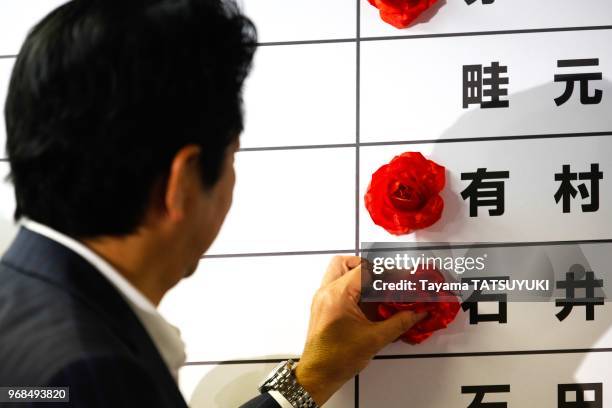 Le Premier ministre du Japon et chef du Parti liberal, Shinzo Abe, pose une rose sur le nom du candidat vainqueur lors du depouillement du scrutin...