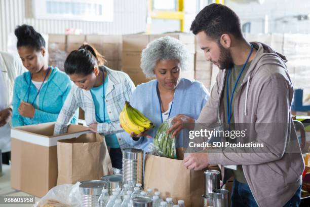 diverse group of volunteers in food bank - packing food stock pictures, royalty-free photos & images