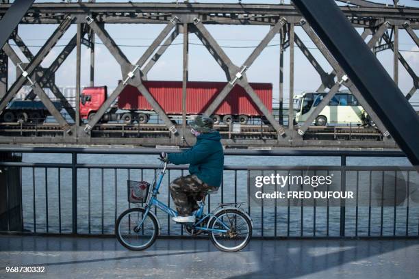 This picture taken on May 29, 2018 shows a Chinese worker riding her bike on the Broken Bridge in the border city of Dandong, in China's northeast...