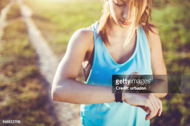 een jonge vrouw kijkt naar het horloge na het lopen. - fitness armband stockfoto's en -beelden