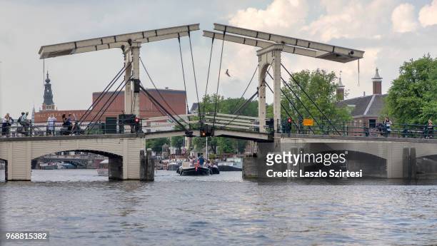 Sightseeing boats pass under the Magere Brug Bridge on May 30, 2018 in Amsterdam, Netherlands. This moveable bridge over the Amstel river is the...