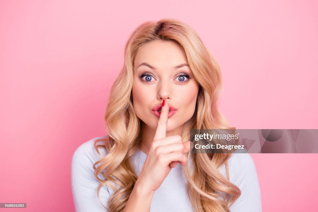 Shhh! Ritratto di ragazza piuttosto misteriosa in abito casual che mostra il segno del silenzio che tiene l'indice sulle labbra con i capelli ricci acconciatura moderna isolata su sfondo rosa