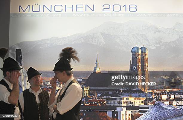 Three men in traditional Bavarian costumes talk in front of a poster promoting the 2018 Winter Olympics in Munich during the "Bavarian Night" at the...