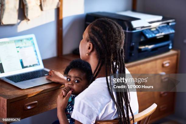 mother with baby son working on laptop - frau zopf hinten stock-fotos und bilder