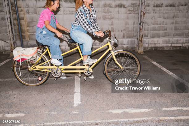 two young woman trying to ride a tandem bicycle - velo humour stock-fotos und bilder
