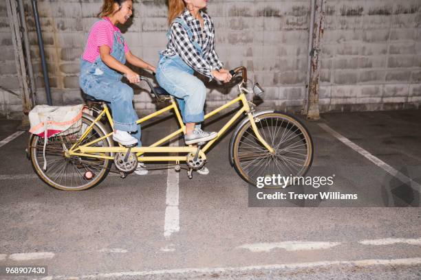 two young woman trying to ride a tandem bicycle - tandem bicycle photos et images de collection