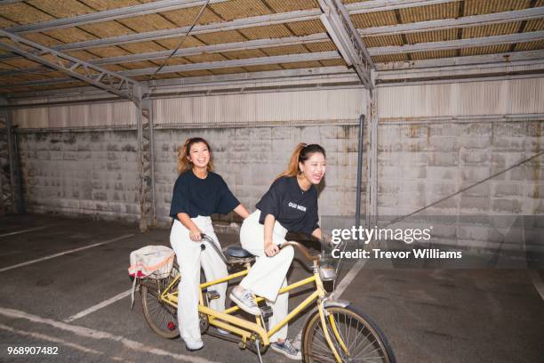 two young woman trying to ride a tandem bicycle - ciclismo tandem fotografías e imágenes de stock