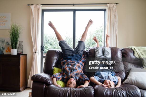 los niños en la casa divertirse estar boca abajo en el sofá en sala de estar. - polynesian culture fotografías e imágenes de stock