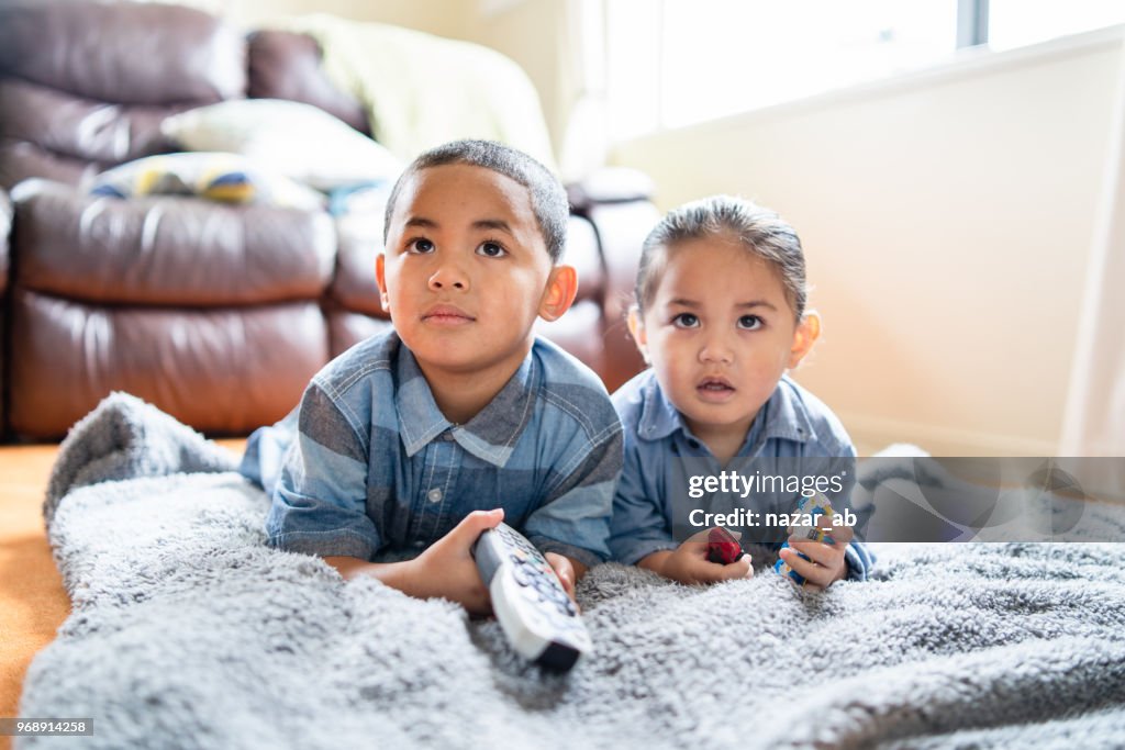 Two brothers lying down and watching TV.