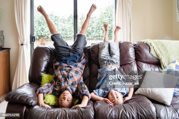 kinderen thuis plezier wordt ondersteboven op sofa in de woonkamer. - polinesische cultuur stockfoto's en -beelden