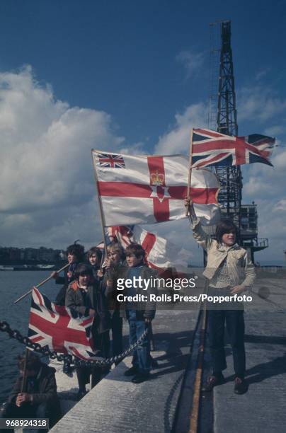 View of young boys waving union flags and red and white Ulster red hand banner flags as they prepare to take part in a junior Orange Order Easter...