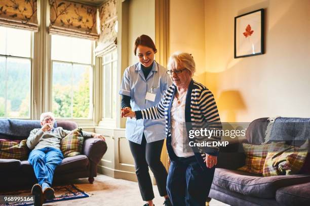 verpleegkundige ondersteunende oude vrouw binnenshuis lopen - welfare stockfoto's en -beelden