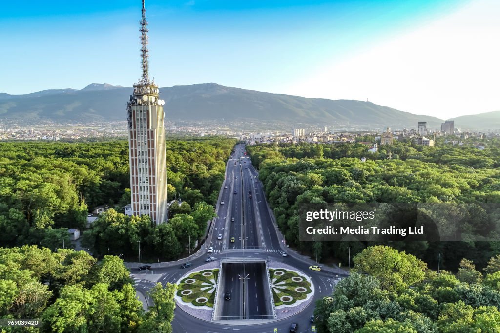 Drone shot of traffic circle and radio tower in the middle of a beautiful city forest