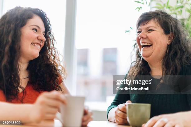 two sisters or siblings having a discussion and laughing inside a cafe - sister stock pictures, royalty-free photos & images