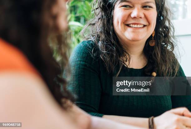 two sisters or siblings having a discussion at a table and listening with a smile - sister stock pictures, royalty-free photos & images