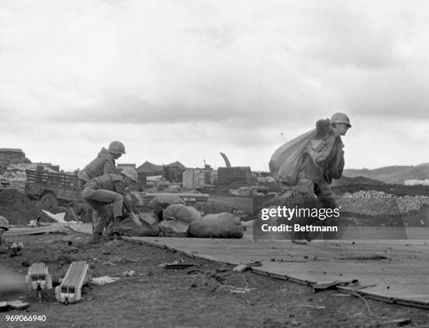 Framed by barbed wire, a lone Marine stands guard with a machine gun in a bunker on the perimeter of this fortress. North Vietnamese artillerymen...