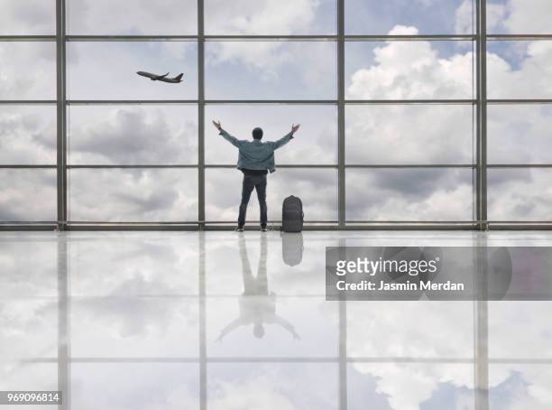 man at airport terminal looking at airplane flying - jasmin merdan stock pictures, royalty-free photos & images
