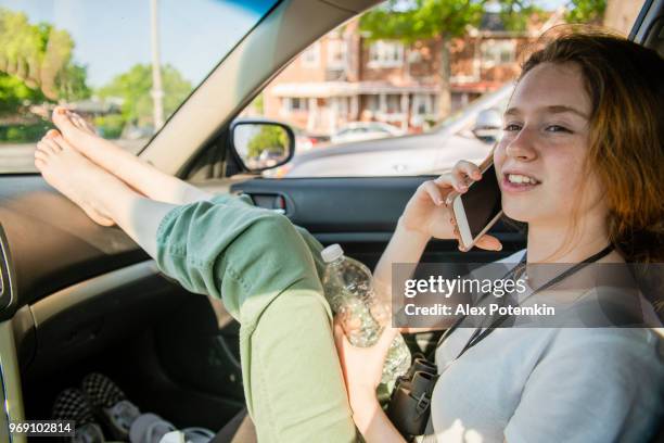 de aantrekkelijke vrolijke langharige kaukasische jong meisje praten via smartphone en rust op de passagiersstoel in de auto tijdens de road trip - beautiful barefoot girls stockfoto's en -beelden