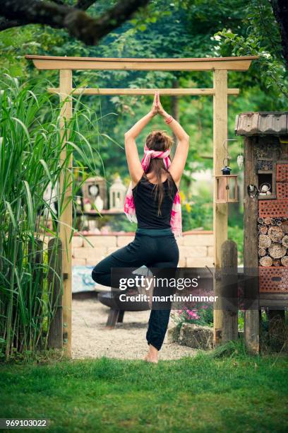 vrouw yoga praktijken en mediteert in de tuin onder een japanse gate - martinwimmer stockfoto's en -beelden