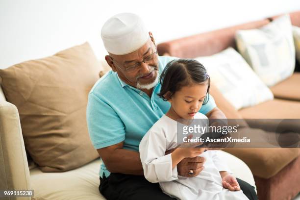 senior muslim man with his granddaughter using an e-reader - two young arabic children only indoor portrait stock pictures, royalty-free photos & images