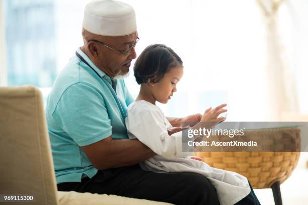 senior muslim man with his granddaughter using an e-reader - two young arabic children only indoor portrait stock pictures, royalty-free photos & images