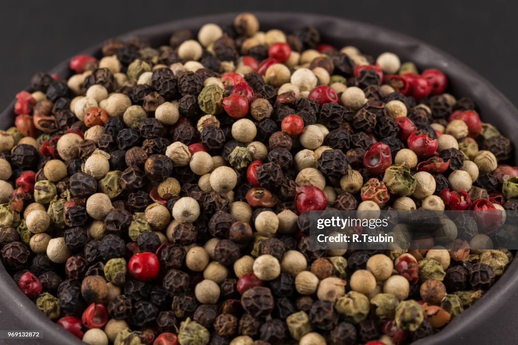 Bowl of various pepper peppercorns seeds mix on dark stone