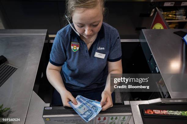 An employee places Hungarian one thousand forint currency banknotes into the cash register at the check-out area inside a Lidl Ltd. Grocery store in...