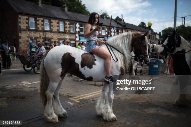 Woman checks her phone as she rides a horse on The Sands street on the opening day of the annual Appleby Horse Fair, in the town of...