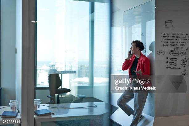 silhuet of businesswoman talking on the phone in office with glass walls - red blazer stock pictures, royalty-free photos & images