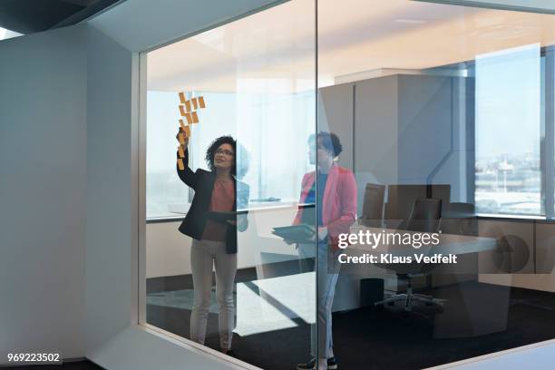 businesswomen putting notes on glass wall inside corner office - corner office stock pictures, royalty-free photos & images