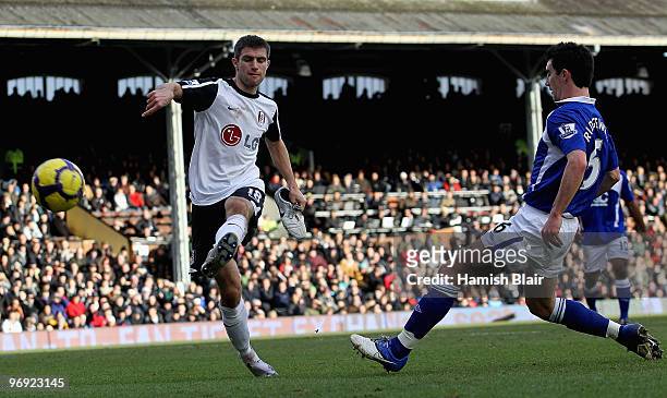 Aaron Hughes of Fulham clears the ball away from Liam Ridgewell of Birmingham with his other boot in his hand during the Barclays Premier League...