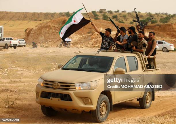 Syrian rebel fighters wave and gesture with machine guns while standing in the back of a pickup truck during a military parade near the southern city...