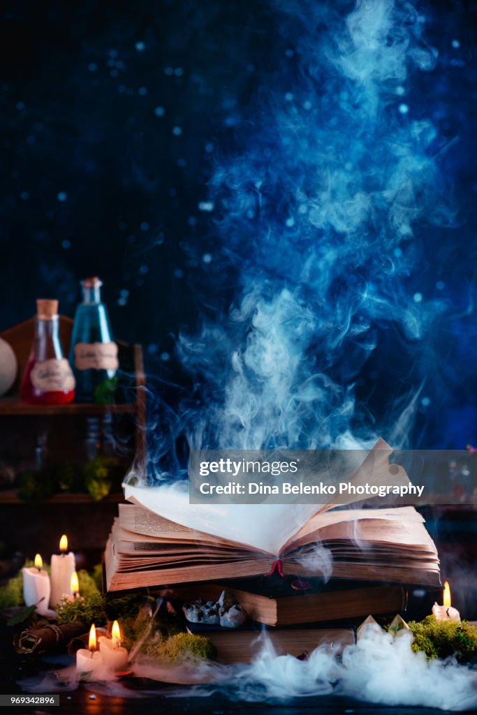 Magical spell book with mysterious smoke. Witch workplace with potions and herbs. Open book on a dark background with copy space