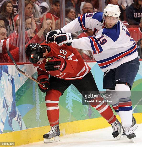 Michael Richards of Canada is checked by Ryan Whitney of the United States during the ice hockey men's preliminary game between Canada and USA on day...