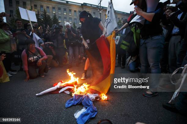 Protesters burn an American flag and a German national flag outside the National Assembly of Quebec during a demonstration ahead of the Group of...