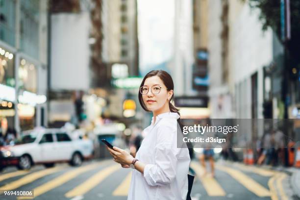 portrait of smart asian businesswoman using mobile phone in busy downtown city street - central asia stock-fotos und bilder