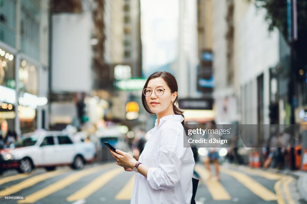 Portrait of smart Asian businesswoman using mobile phone in busy downtown city street