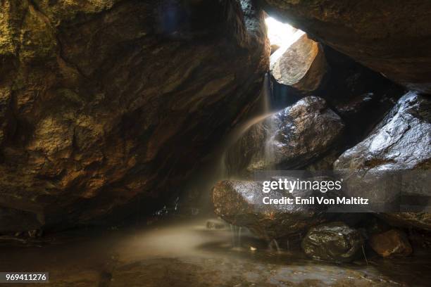 a sunlit rough hewn cavern with a gush of water in the royal natal drakensberg, amphitheatre, ukhahlamba national park, kwazulu-natal, south africa - rock hewn stock pictures, royalty-free photos & images