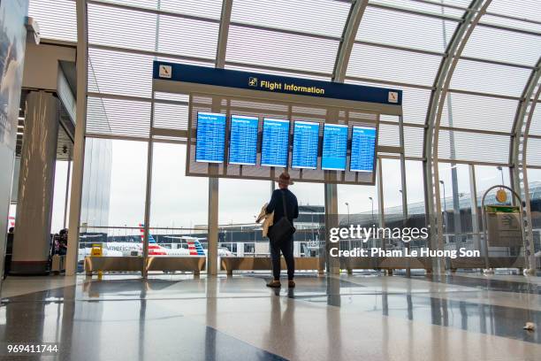 man looking for flight at timetable in departure lounge of o'hare international airport - le lounge stockfoto's en -beelden